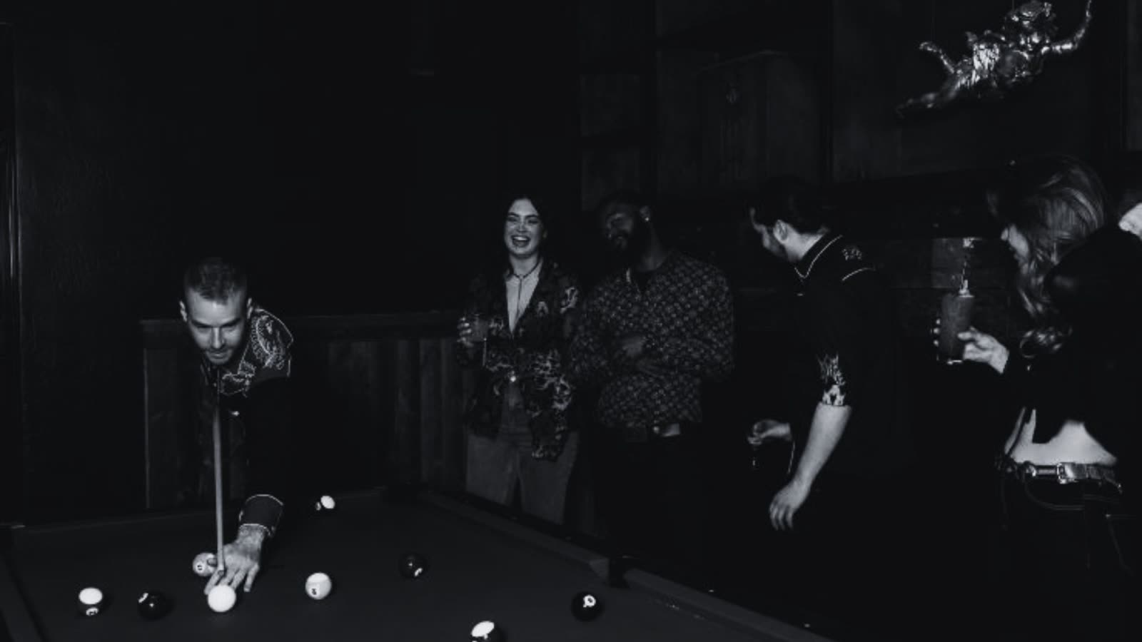 Friends gathered around a billiards table in a moody lounge.