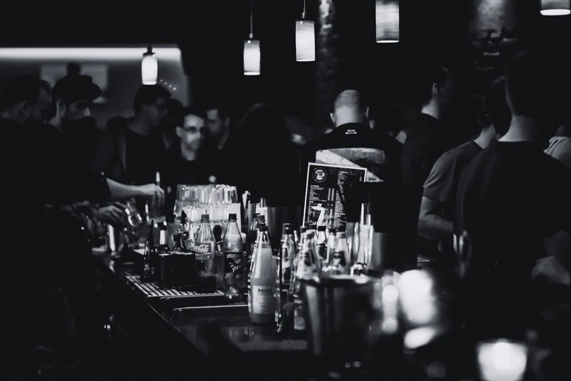 A bar in motion — bottles, pendant lights, and a crowd gathered close.